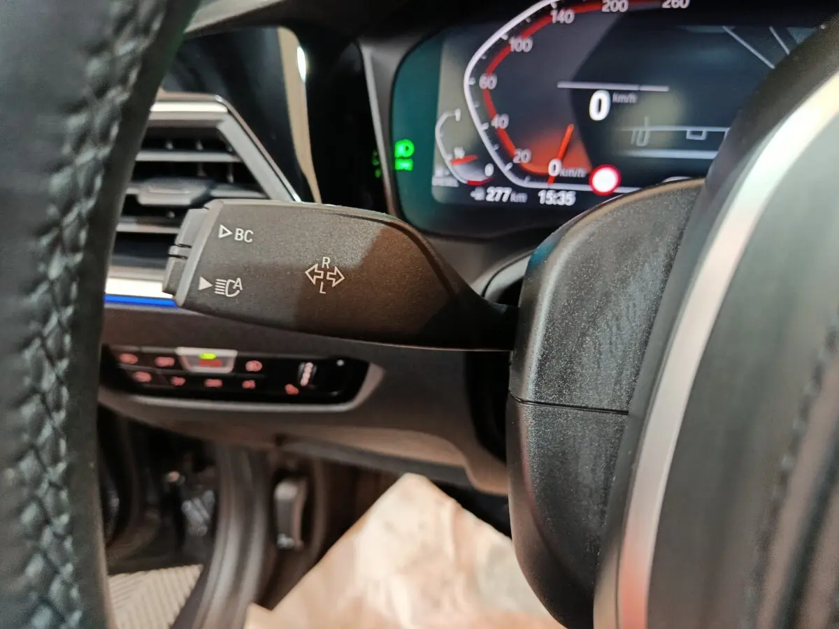 Gros plan sur la manette de clignotant à gauche du volant noir, avec tableau de bord numérique BMW Série 3 318d.