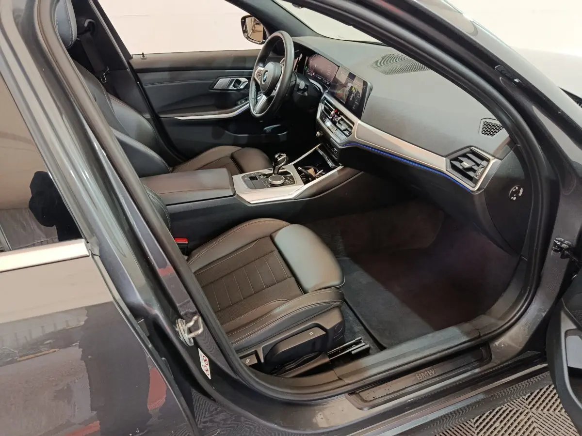 Vue intérieure côté conducteur d'une BMW Série 3 318d grise, avec tableau de bord moderne et sièges en cuir noir.