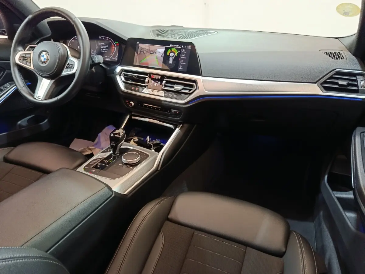 Vue intérieure côté conducteur de la BMW Série 3 318d Lounge 2022, avec tableau de bord digital et éclairage d'ambiance bleu.