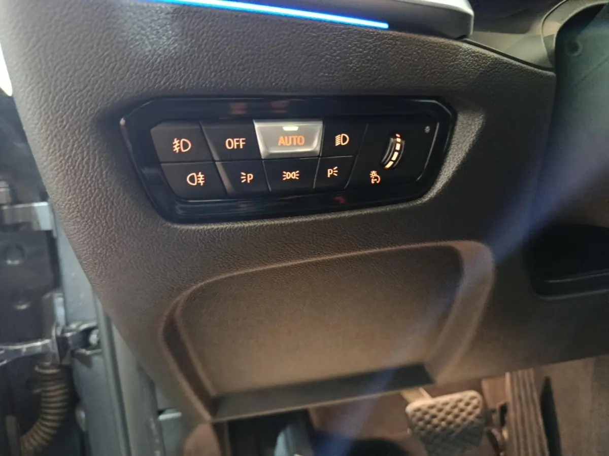 Gros plan sur les commandes d’éclairage à gauche du volant dans une BMW Série 3 gris clair 318d Lounge 2022.