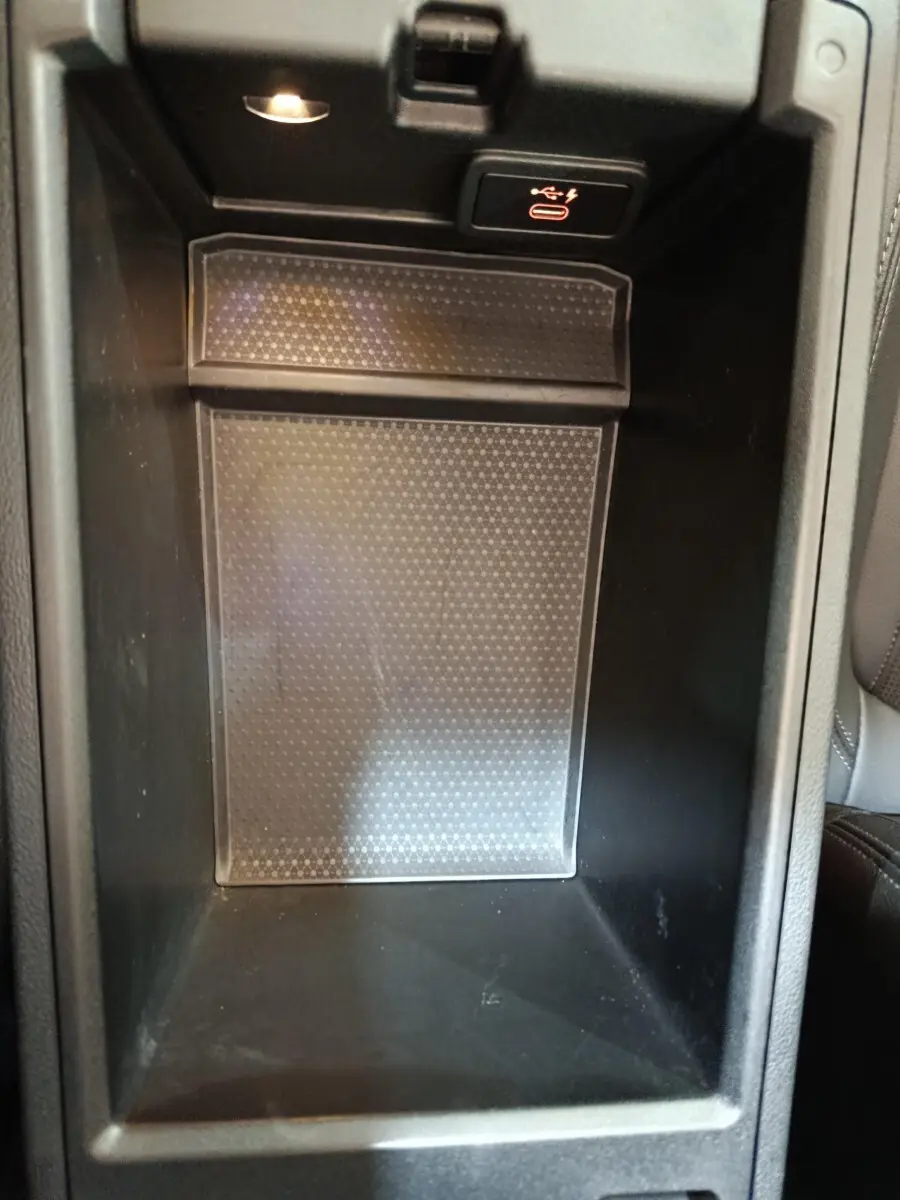 Gros plan sur le compartiment de rangement central noir avec port USB et recharge sans fil dans une BMW Série 3 gris clair.