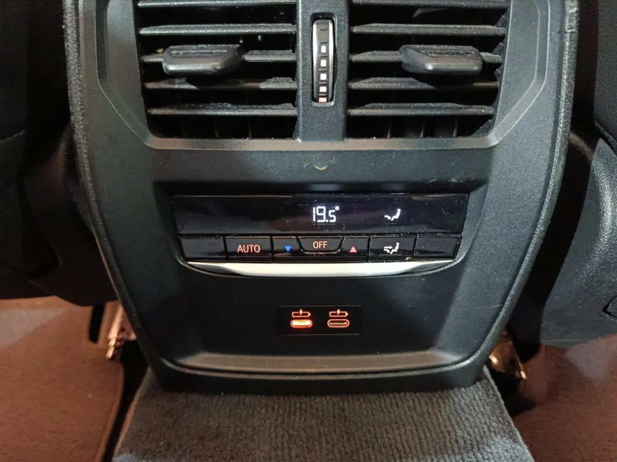 Détail de la console arrière noire avec commandes climatisation digitale et prises USB rouges sur BMW Série 3 gris clair.