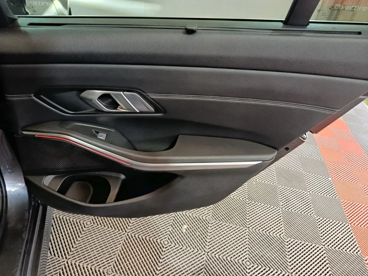 Vue intérieure du panneau de porte côté conducteur de BMW Série 3 gris clair, avec poignée argentée et bande lumineuse rouge.