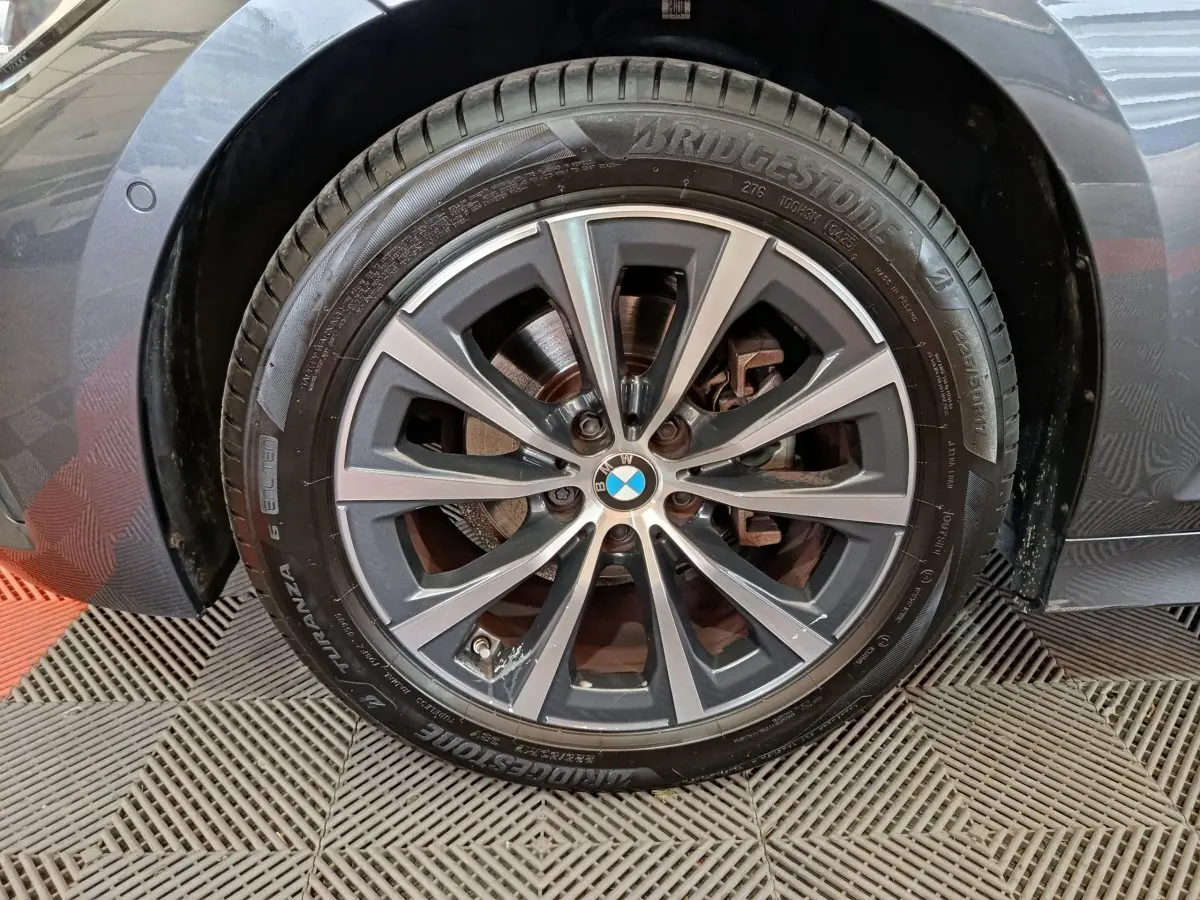 Gros plan sur la roue avant gauche grise d’une BMW Série 3 318d avec jante alliage et pneu Bridgestone.