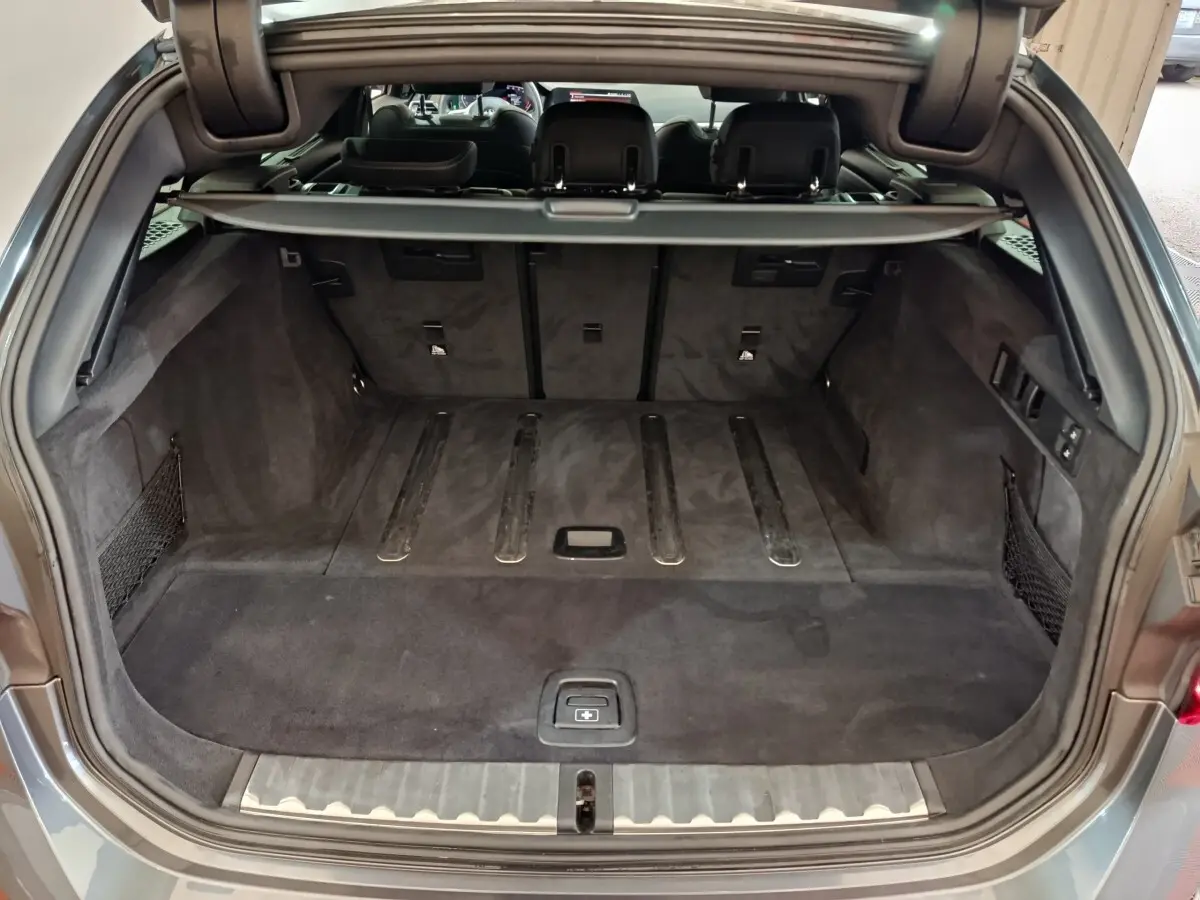 Coffre ouvert vu de l'arrière d'une BMW Série 3 318d gris clair avec intérieur noir et filet de rangement.