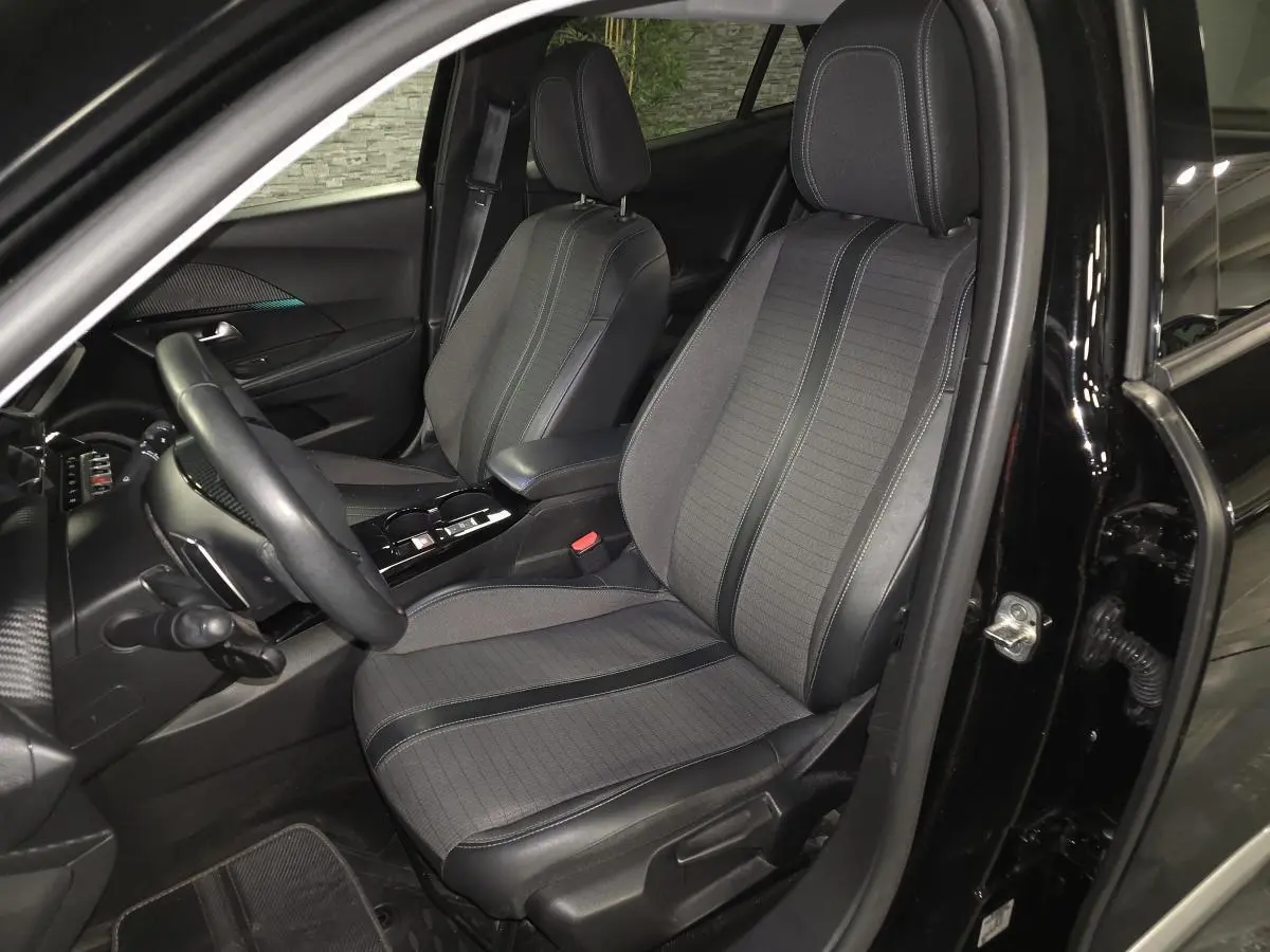 Vue intérieure côté conducteur du Peugeot 2008 noir 2021, sièges tissu et cuir gris avec surpiqûres bleues.