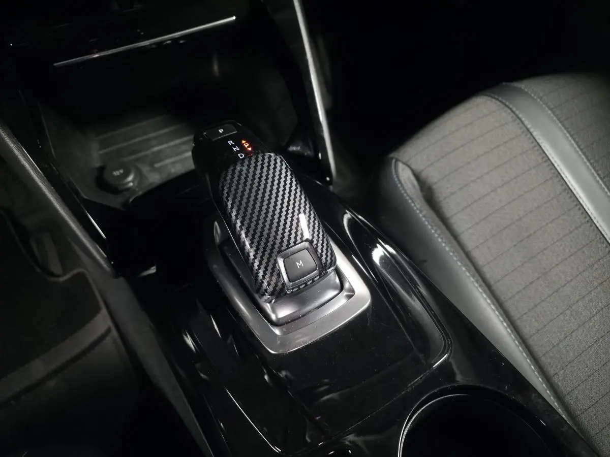 Le levier de vitesse automatique noir à effet carbone de la Peugeot 2008 1.5 BlueHDi, avec siège tissu gris à côté.