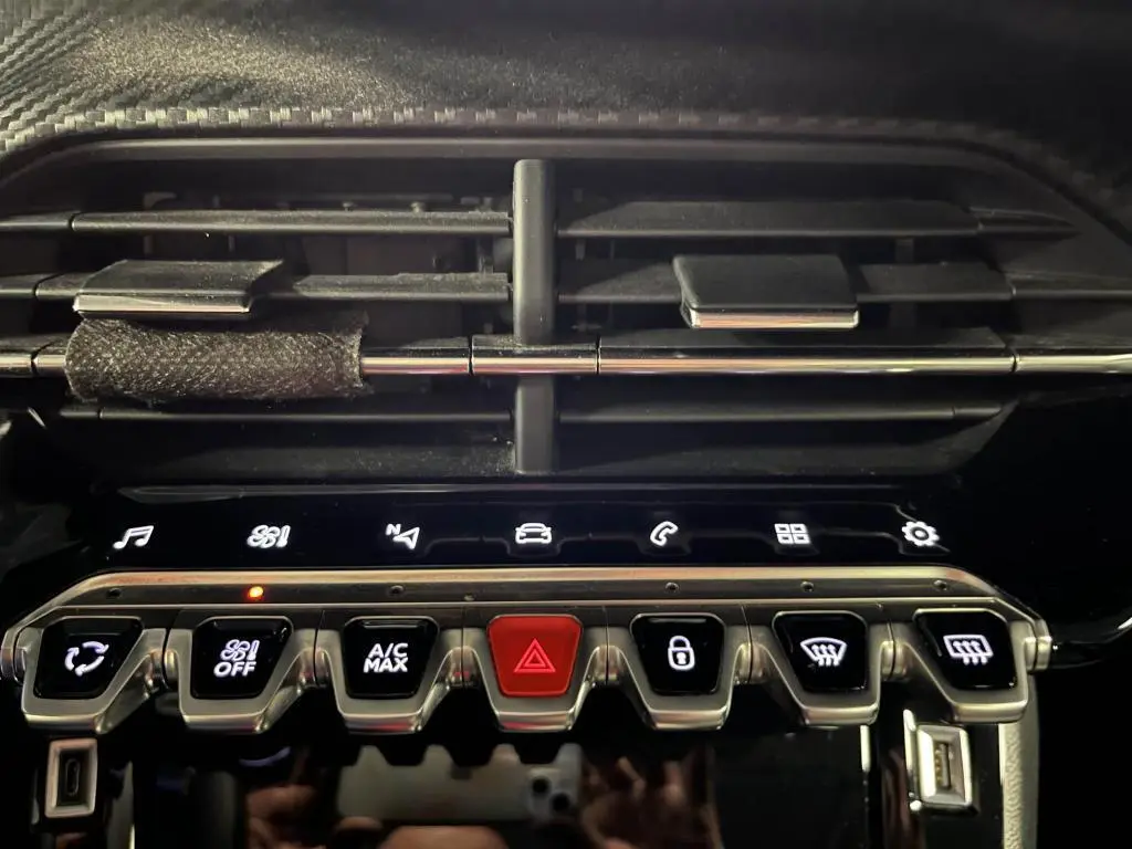 Gros plan sur la console centrale du Peugeot 2008 noir, avec commandes tactiles et aérateurs horizontaux noirs.