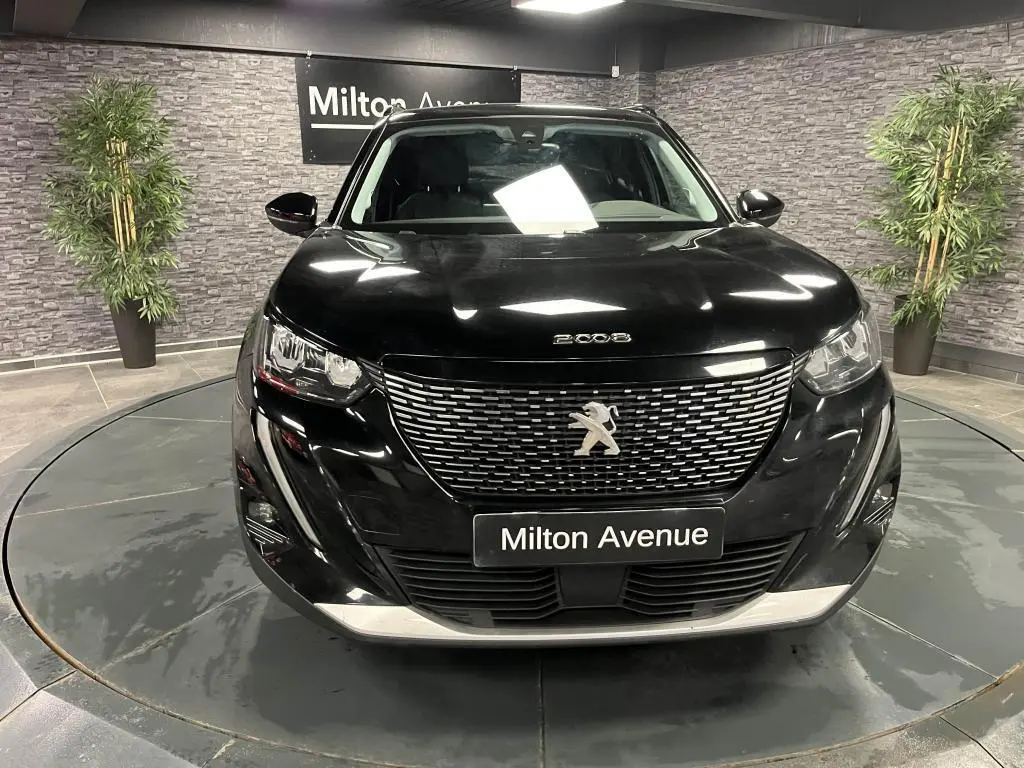 Vue avant d'un Peugeot 2008 noir Perla Nera avec calandre chromée et logo lion sur fond de showroom.