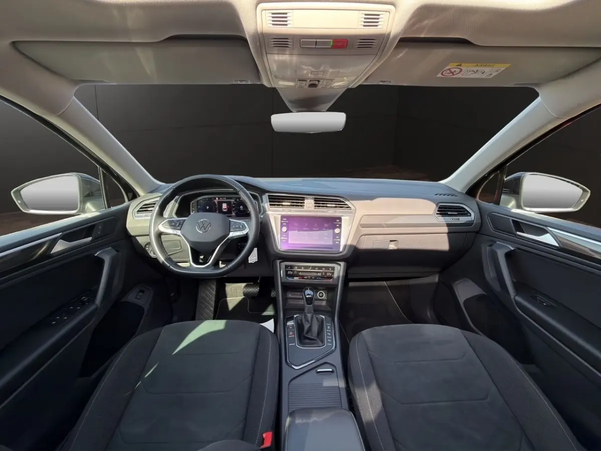 Vue intérieure avant du Volkswagen Tiguan noir 2022, tableau de bord avec écran tactile et volant multifonctions cuir.