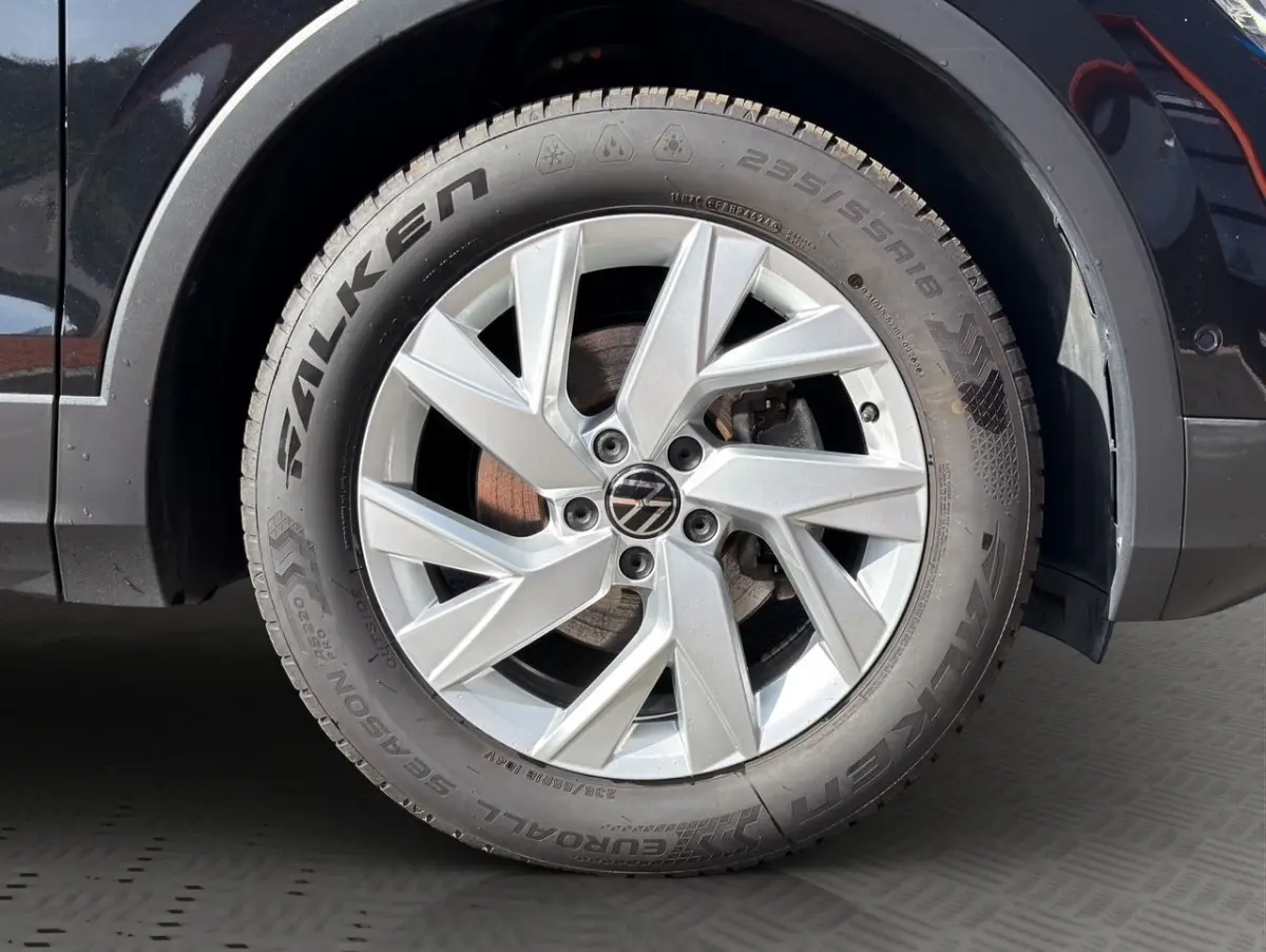 Gros plan sur la roue avant gauche du Volkswagen Tiguan noir, jante alliage argentée avec logo VW central.