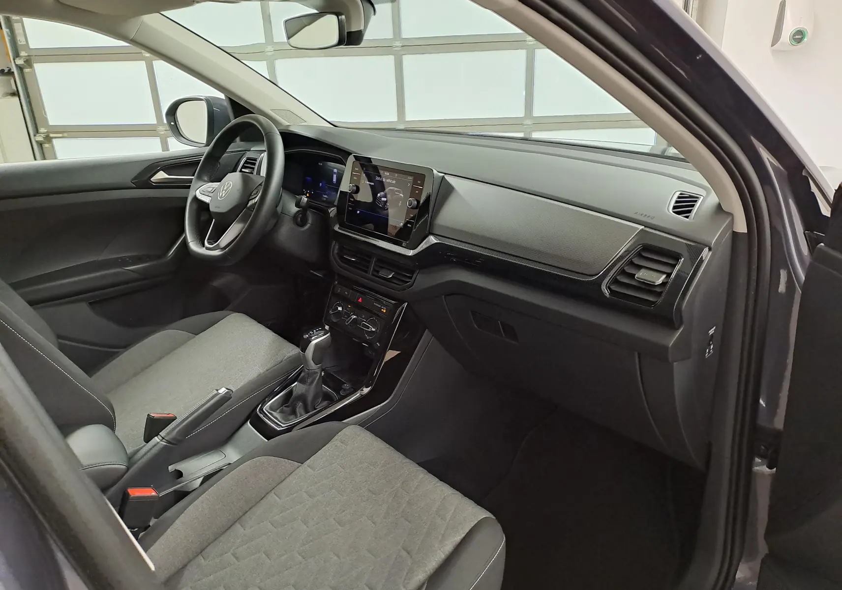Vue intérieure côté conducteur du Volkswagen T-Cross 2025, avec tableau de bord moderne et sièges gris tissu.