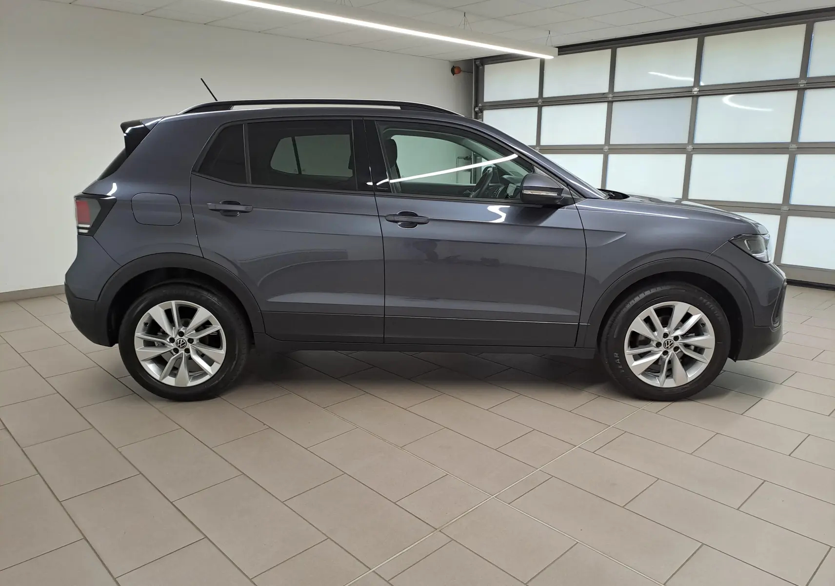 Vue de profil côté gauche d'un Volkswagen T-Cross 2025 gris cendré avec jantes alliage et toit noir.