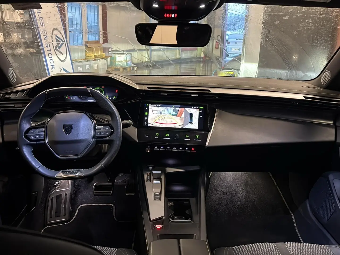Intérieur noir de la Peugeot 408 Hybrid 145 GT, vue de face sur le tableau de bord avec écran tactile et volant cuir.
