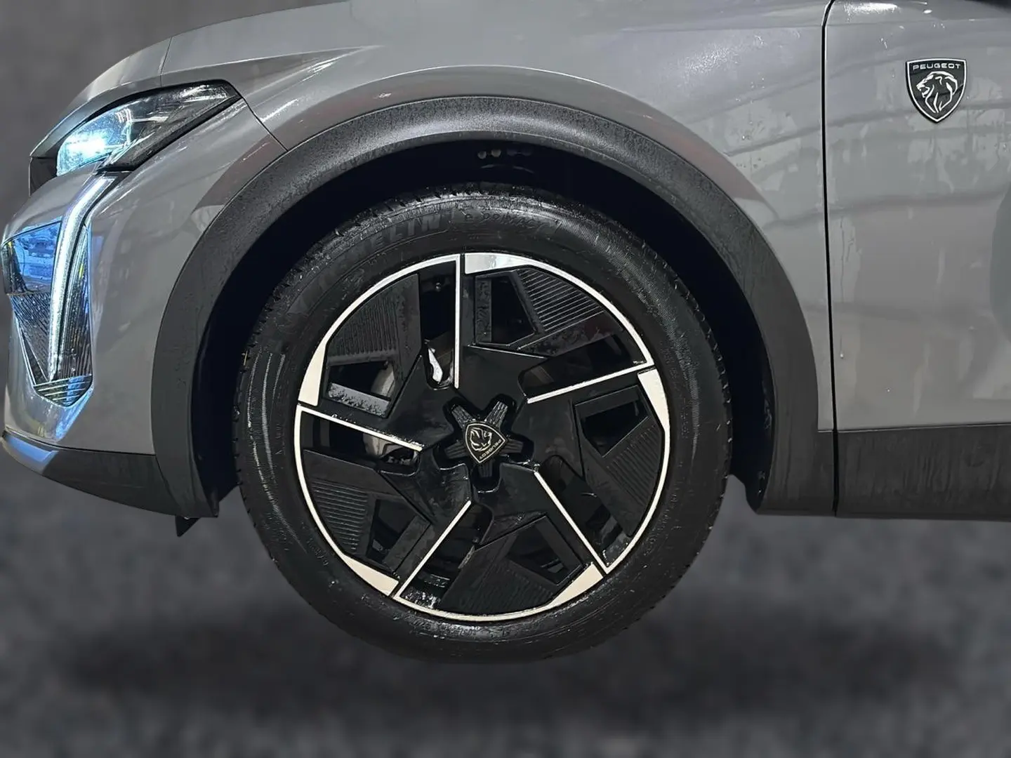 Gros plan sur la roue avant droite et le logo Peugeot d’une 408 Hybrid gris sellenium avec phares LED allumés.