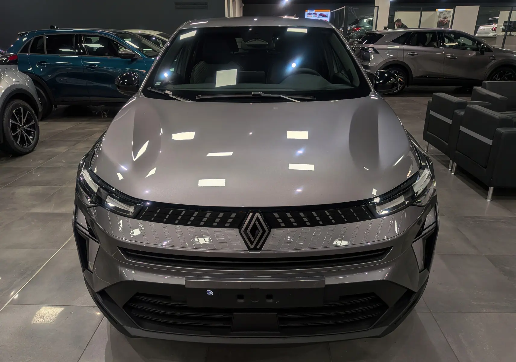Vue frontale d'un Renault Captur 2025 gris Cassiopé avec calandre lumineuse et logo central dans un showroom.