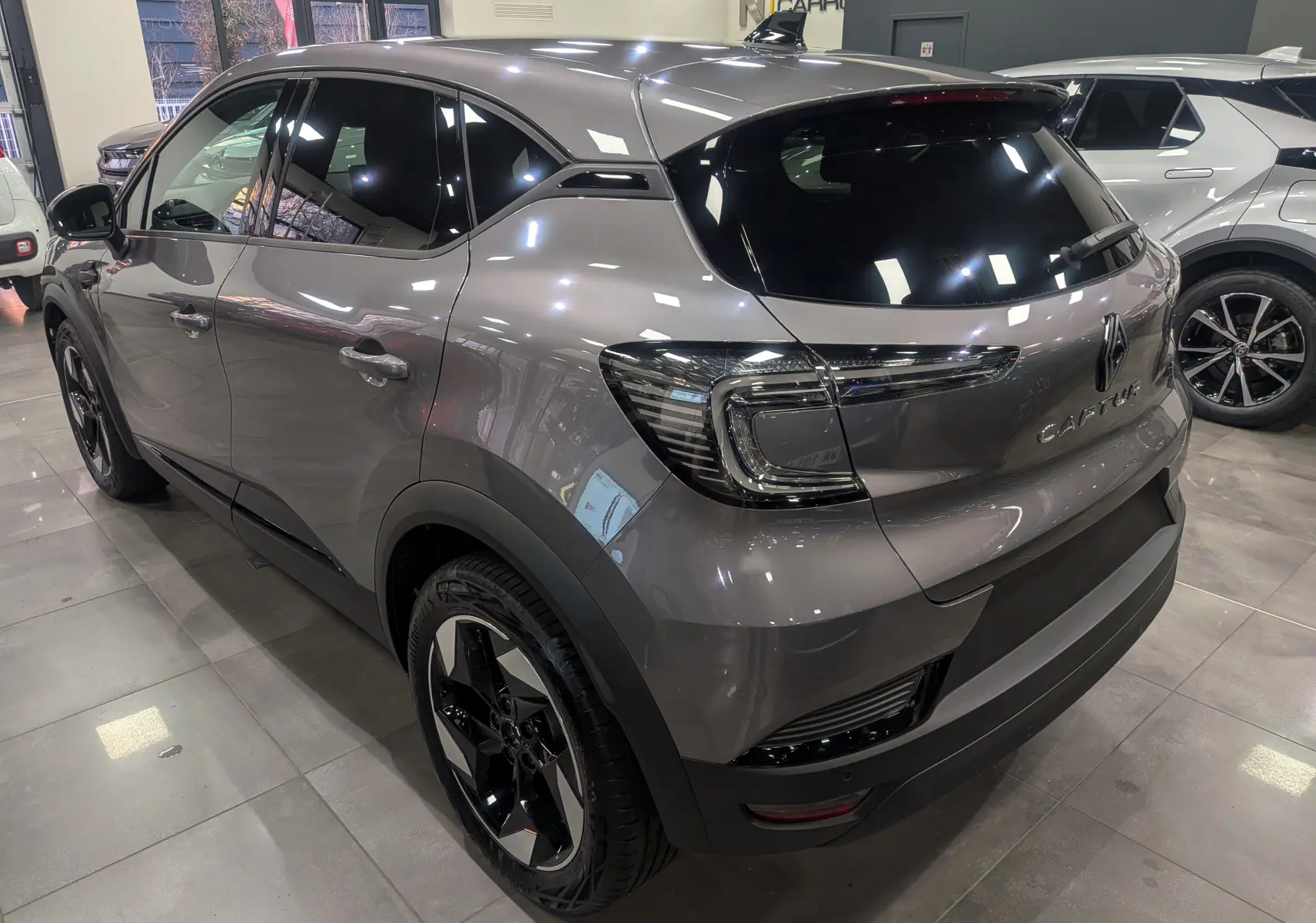 Vue 3/4 arrière droite du Renault Captur gris Cassiopé 2025 avec feux LED et jantes bi-ton noires en showroom.