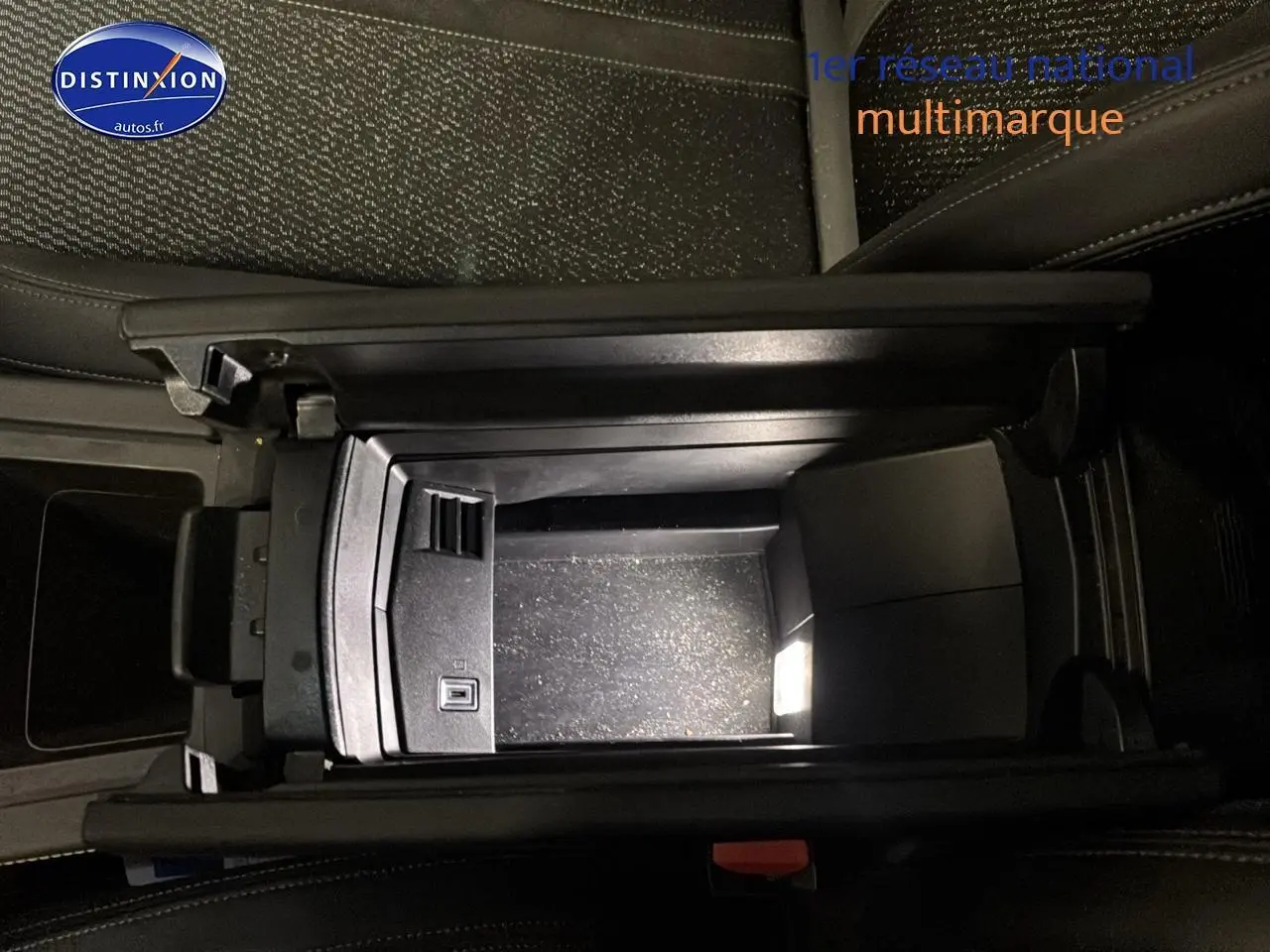 Vue plongeante sur l'accoudoir central ouvert de la Peugeot 408 Hybrid 145 GT gris sélénite, montrant le rangement intérieur.