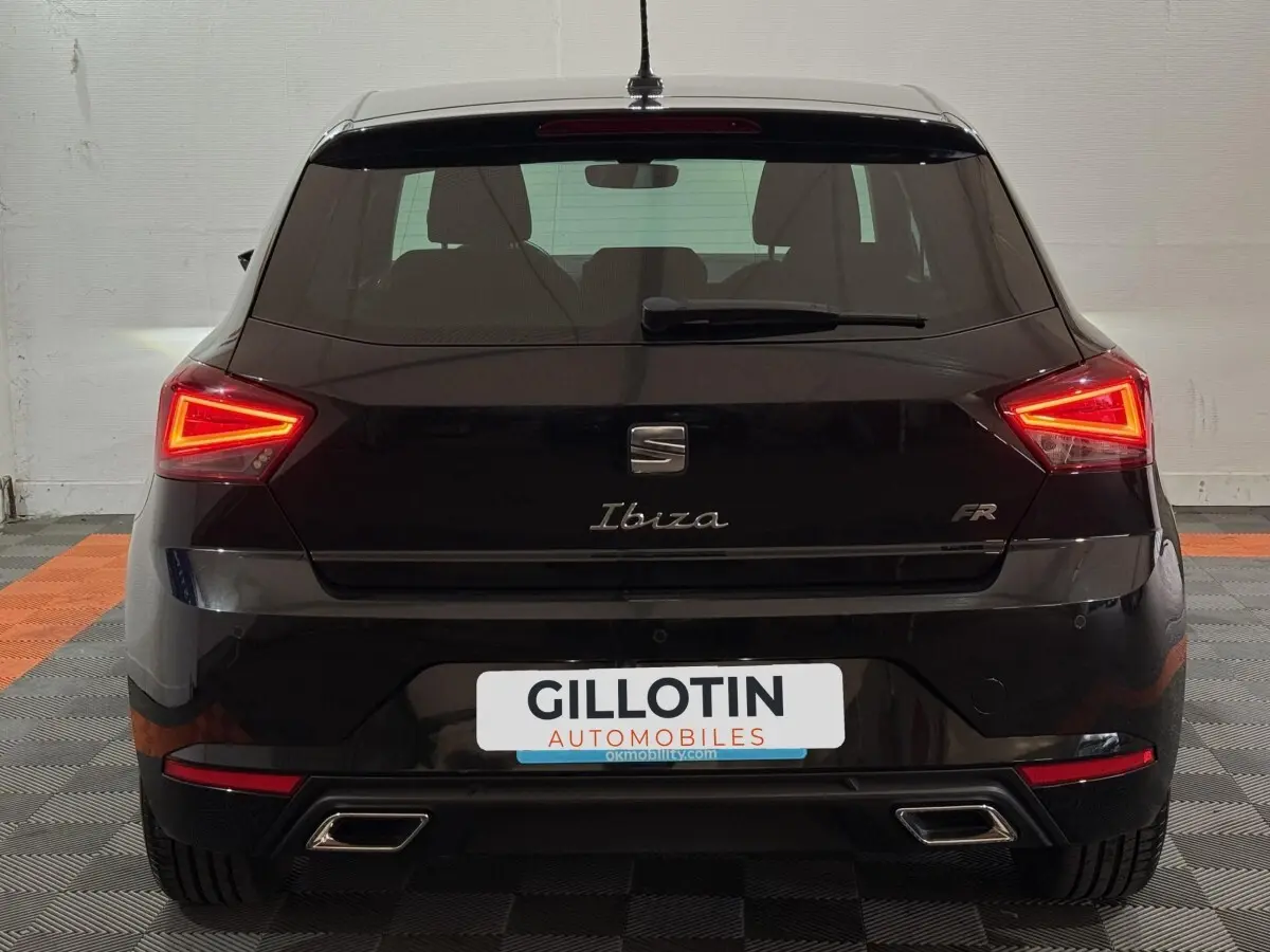 Vue arrière d'une SEAT Ibiza 1.0 TSI 110 FR noire avec feux LED allumés et double sortie d'échappement chromée.