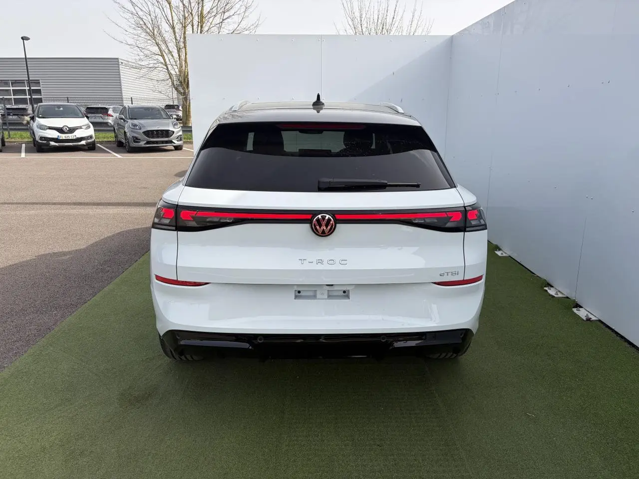 Vue arrière du Volkswagen T-Roc blanc pur avec toit noir et bandeau lumineux LED reliant les feux arrière.