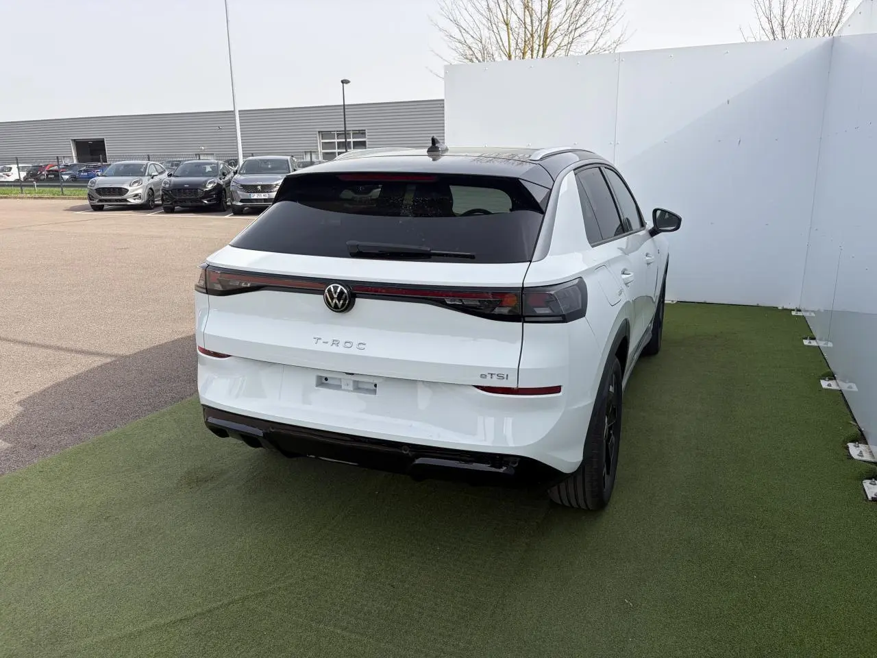 Vue 3/4 arrière droite du Volkswagen T-Roc blanc pur avec toit noir et feux arrière LED reliés par un bandeau lumineux.