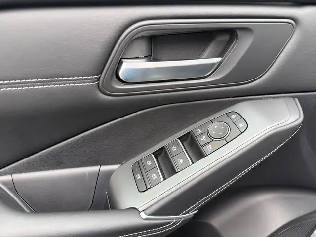 Gros plan sur la porte côté conducteur du Nissan Qashqai gris foncé, avec commandes des vitres et poignée argentée.