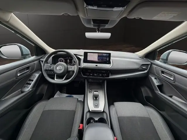 Vue intérieure avant du Nissan Qashqai 2025 gris foncé, avec tableau de bord digital, écran tactile central et volant multifonctions cuir.