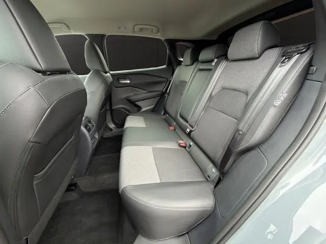 Vue intérieure arrière droite du Nissan Qashqai 2025 gris foncé, montrant la banquette 3 places en tissu et cuir avec ceintures de sécurité.
