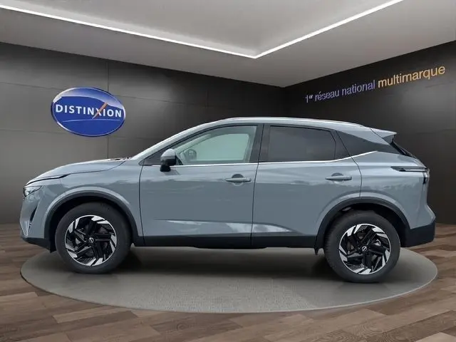 Vue latérale droite d'un Nissan Qashqai gris foncé 2025 en showroom avec jantes noires et toit contrasté gris clair.
