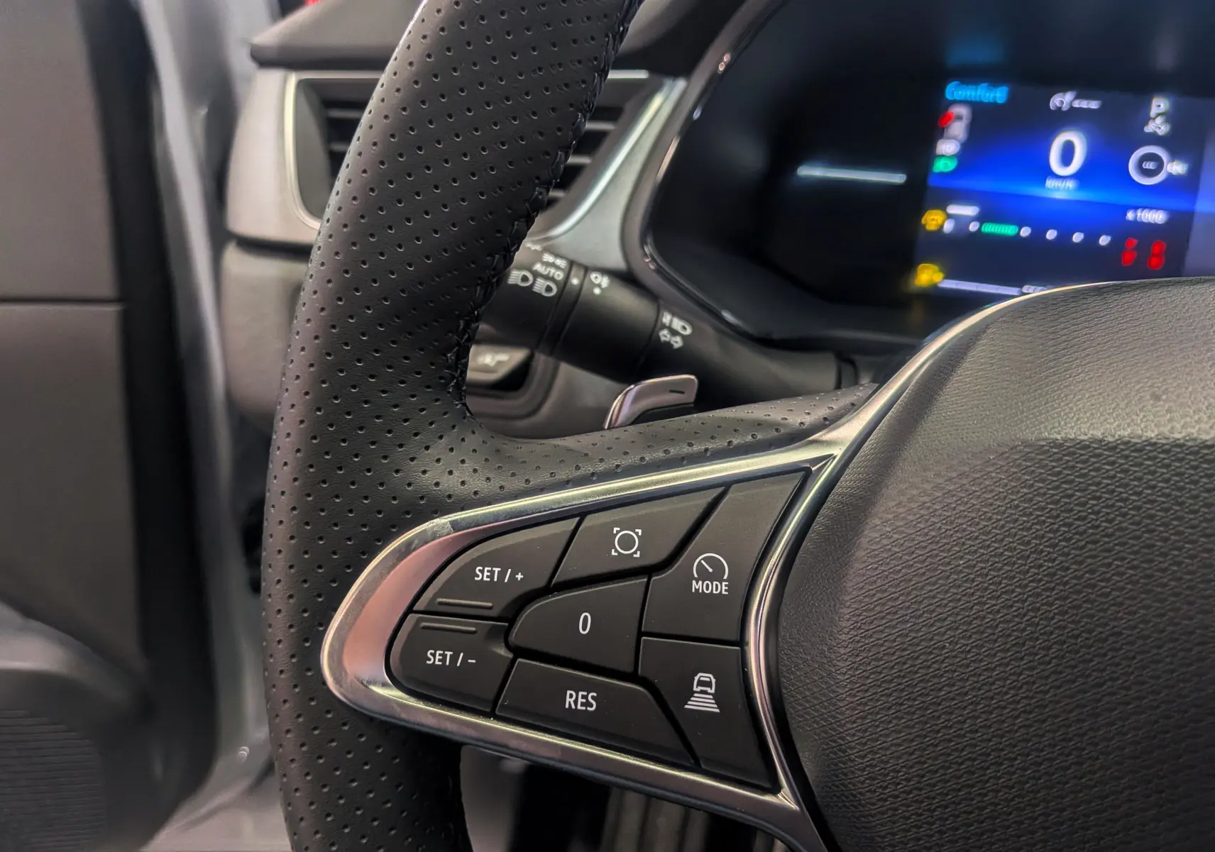 Gros plan sur le volant perforé côté gauche du Renault Captur gris rafale avec commandes de régulateur et tableau de bord numérique.