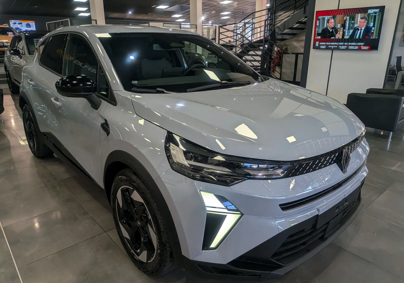 Renault Captur Mild Hybrid gris rafale en 3/4 avant droit, avec feux LED et jantes bi-ton noires visibles en showroom.
