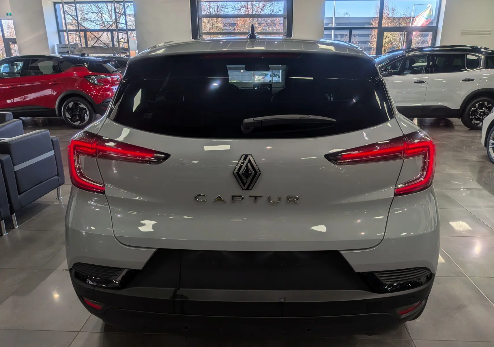 Vue arrière d'un Renault Captur gris rafale 2025 en showroom, avec feux arrière LED allumés et logo central visible.