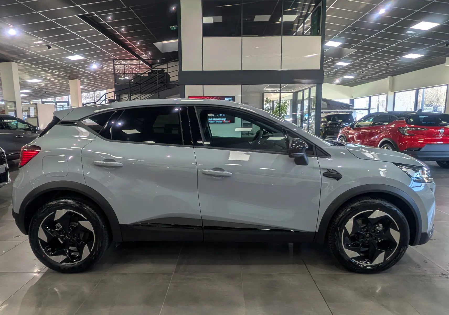 Profil côté droit du Renault Captur 2025 gris rafale avec jantes biton et toit noir en showroom.