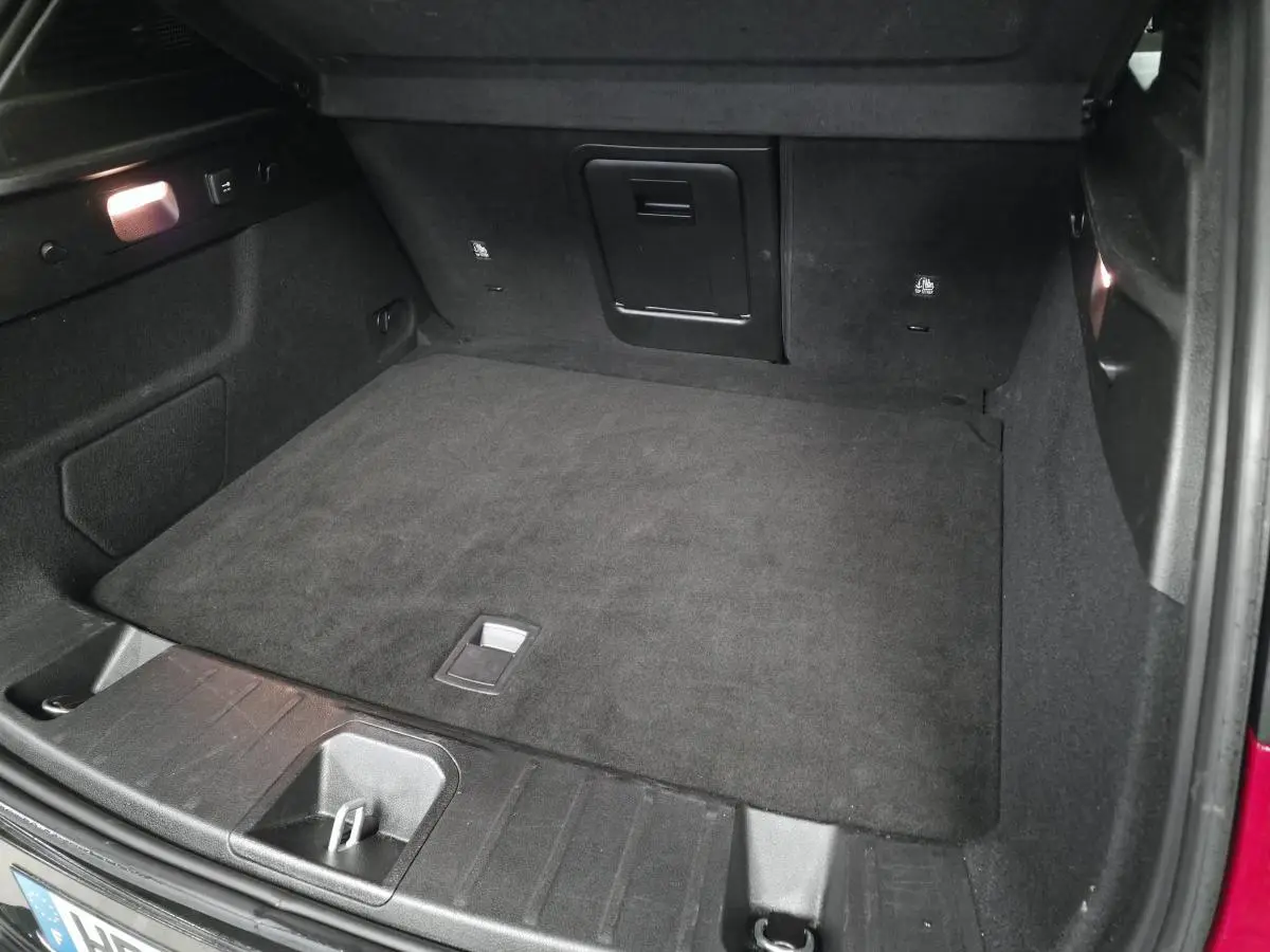 Coffre ouvert de l'Alfa Romeo Tonale rouge 2025, vue intérieure montrant le tapis de sol noir et les rangements.