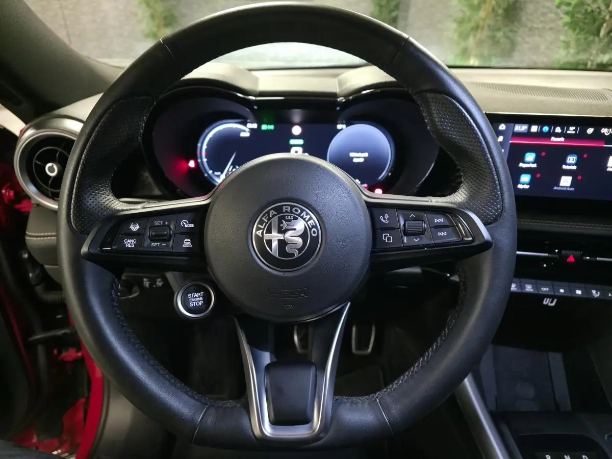 Vue rapprochée du volant sport en cuir noir de l'Alfa Romeo Tonale rouge, avec tableau de bord digital et bouton start visible.