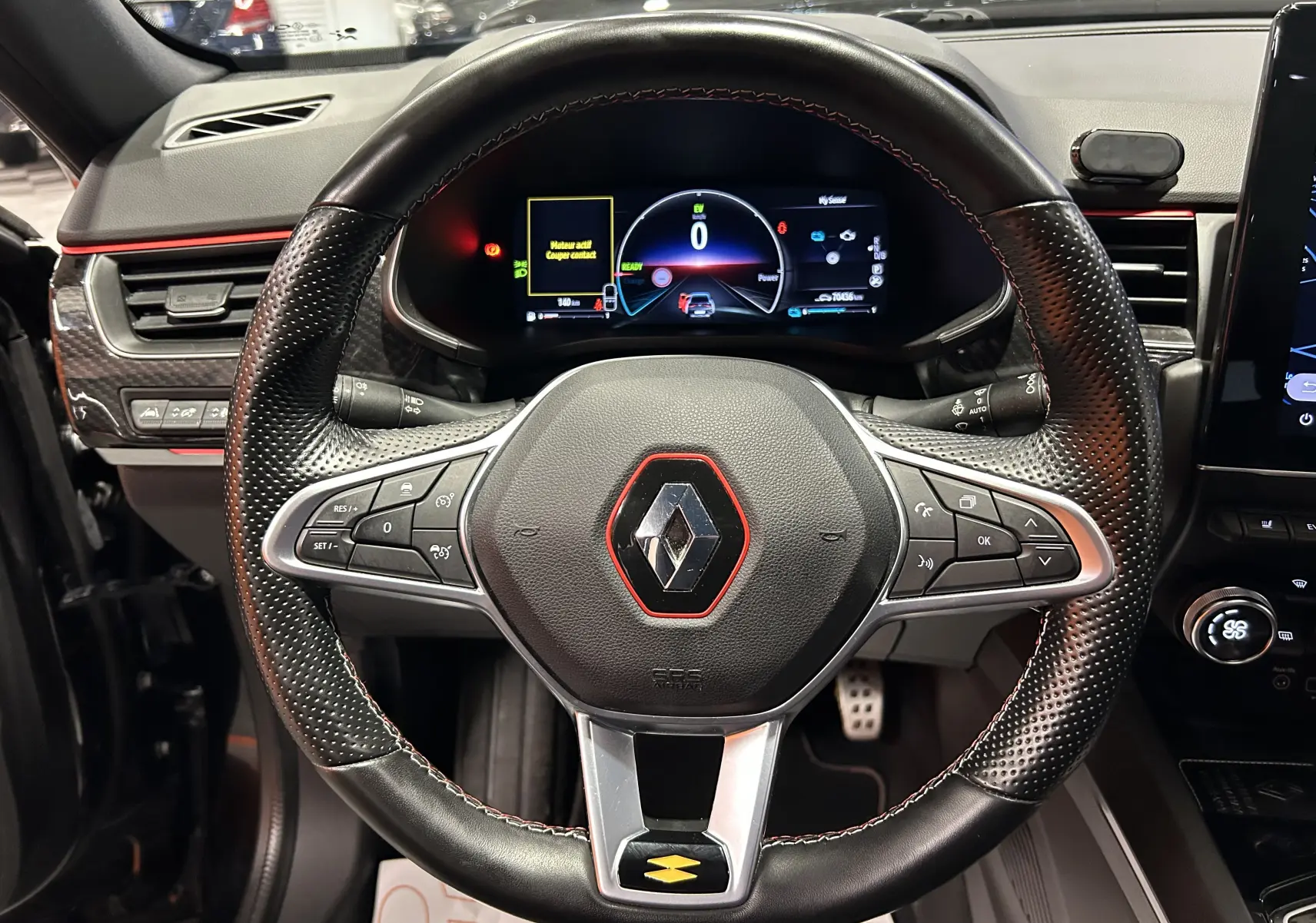 Vue rapprochée du volant noir perforé avec logo Renault rouge et tableau de bord numérique du Renault Arkana E-Tech 2022.