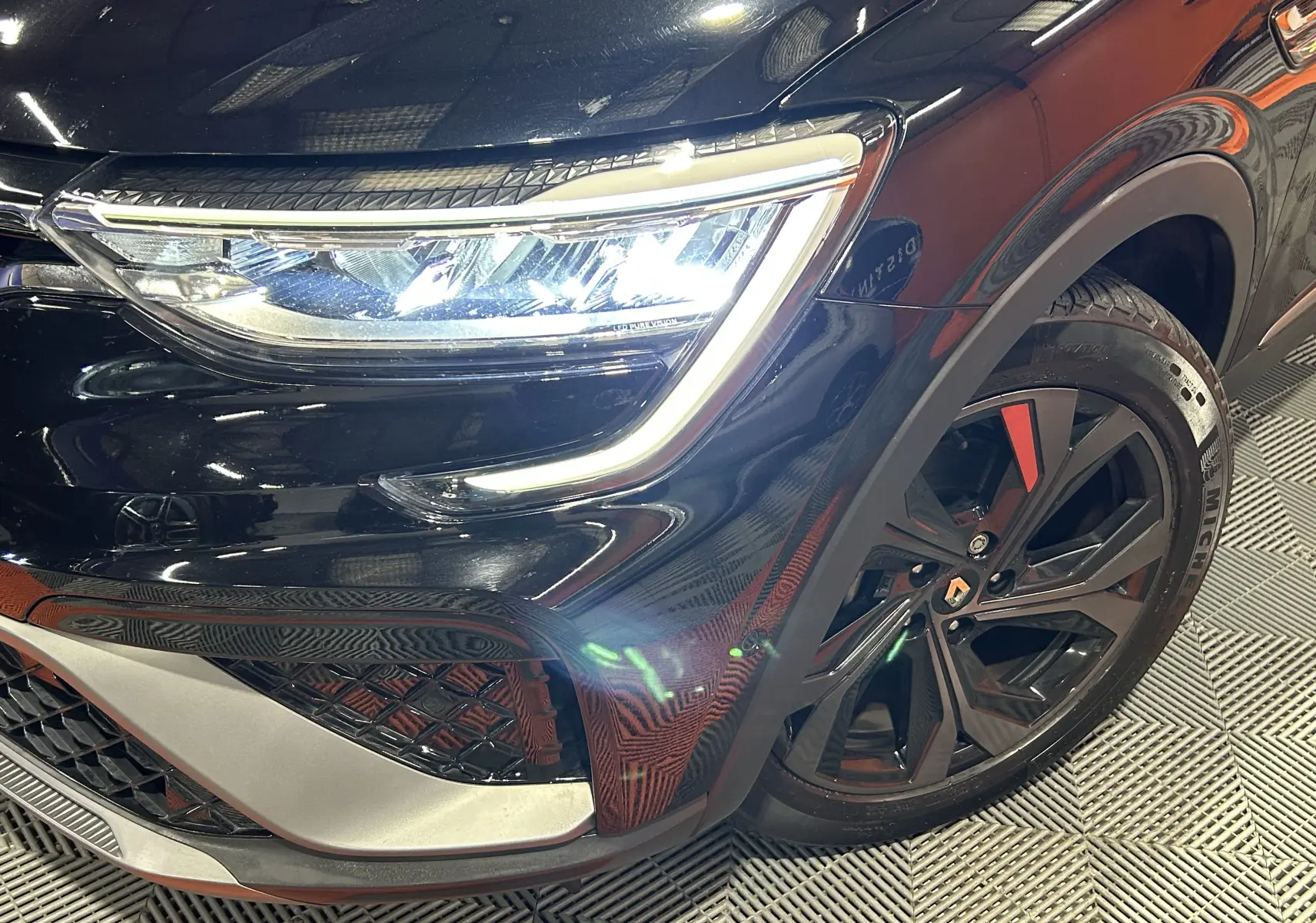 Gros plan sur l'avant droit noir brillant du Renault Arkana E-Tech, mettant en valeur le phare LED et la jante noire à inserts rouges.