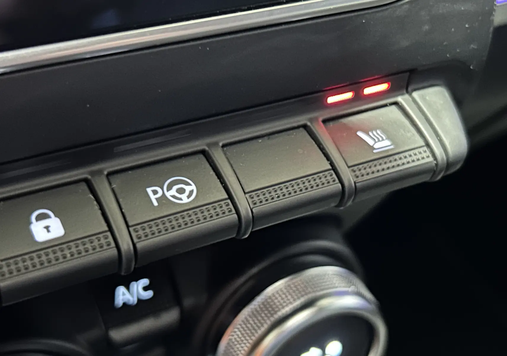 Gros plan sur les boutons de commande du tableau de bord du Renault Arkana noir, avec témoin de siège chauffant allumé.