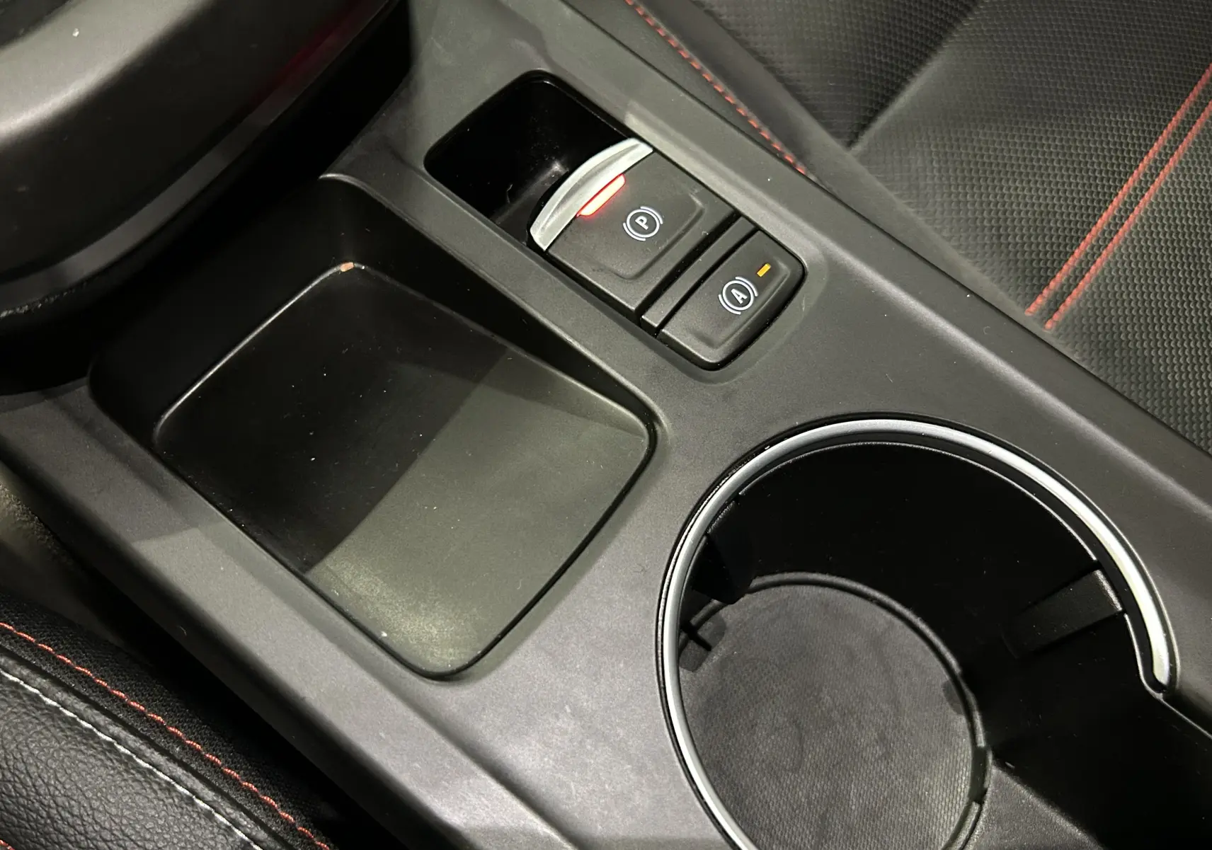 Gros plan sur la console centrale noire du Renault Arkana E-Tech 145ch RS Line 2022 avec porte-gobelet et boutons électroniques.