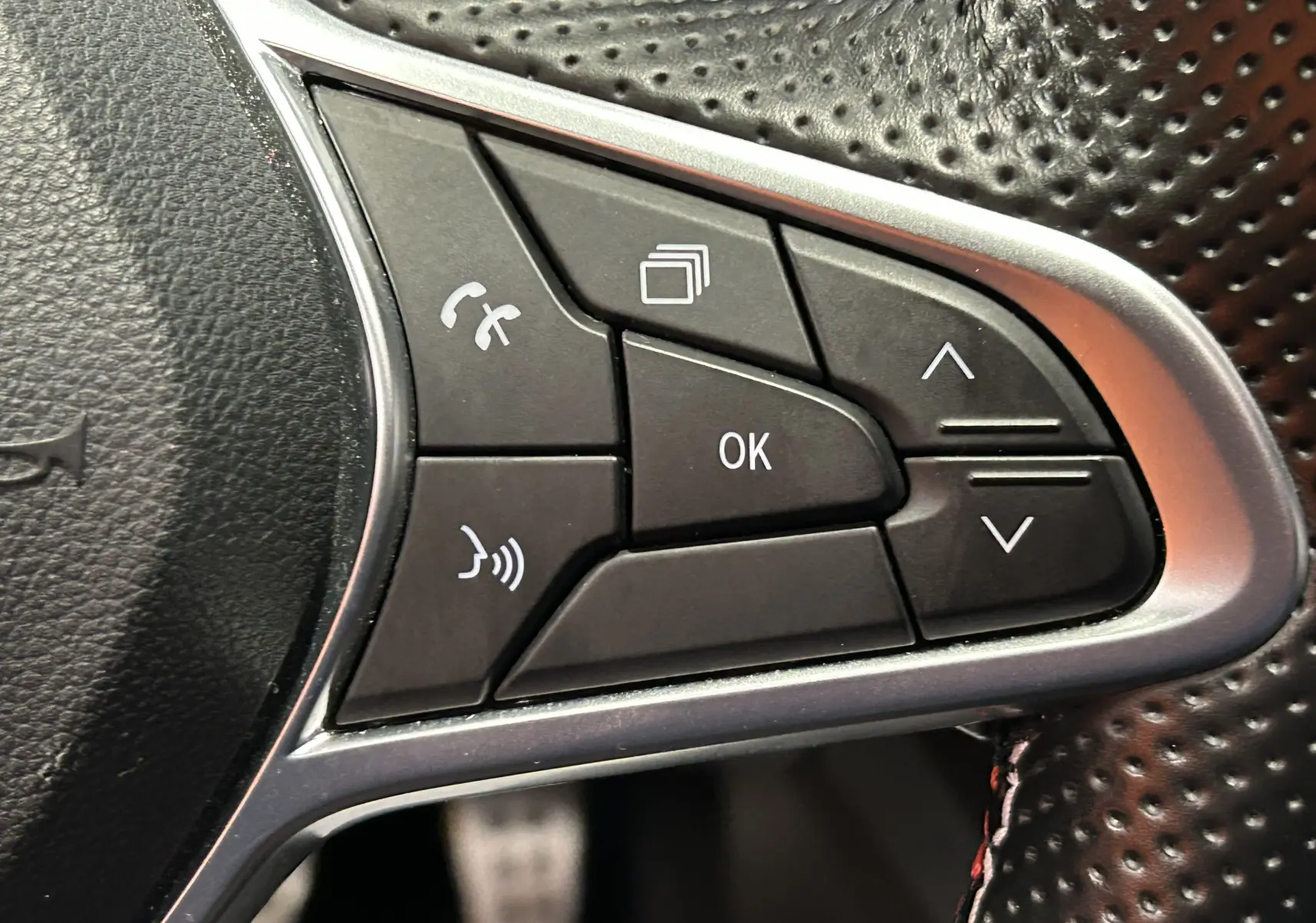 Gros plan sur les commandes multifonctions noires du volant perforé de la Renault Arkana E-Tech noire.