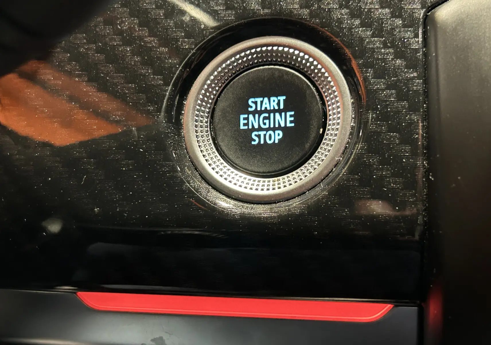 Gros plan sur le bouton Start Engine Stop entouré d’un cadre argenté, sur fond noir brillant avec insert rouge intérieur Renault Arkana.