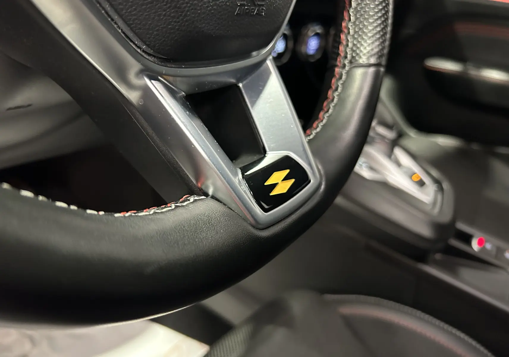 Gros plan sur le volant noir avec surpiqûres rouges et logo jaune, intérieur du Renault Arkana E-Tech 2022.