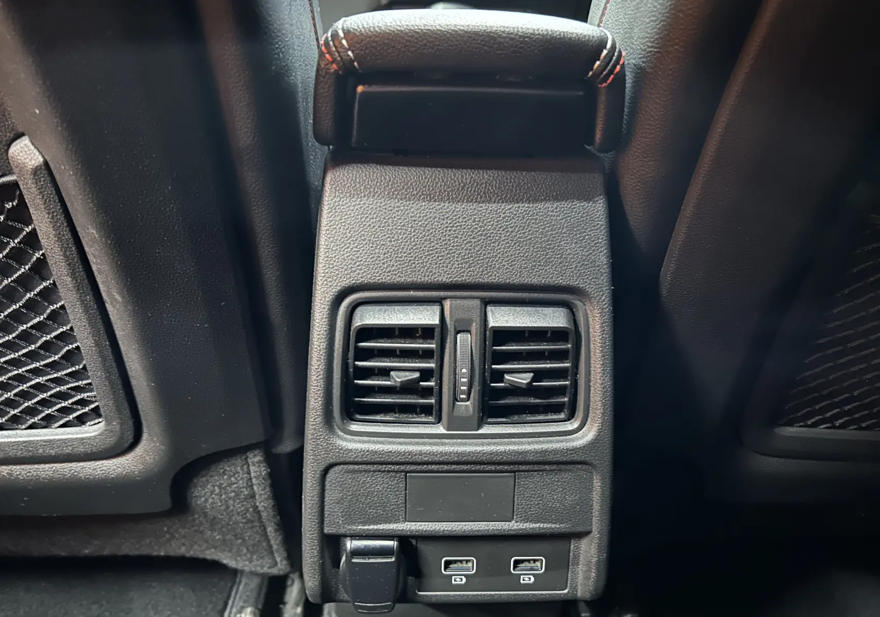 Vue rapprochée des aérateurs arrière et ports USB noirs entre les sièges avant d’un Renault Arkana noir.