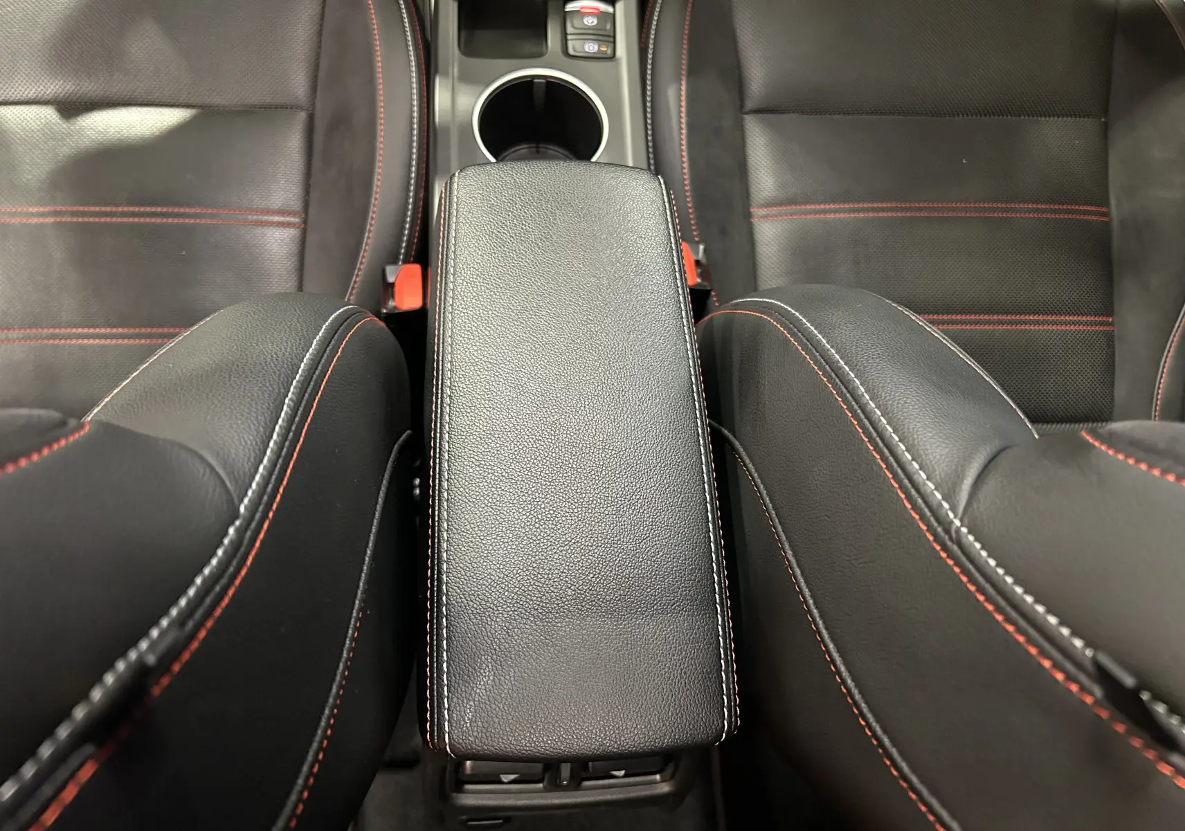 Vue plongeante sur l'accoudoir central noir avec surpiqûres rouges entre les sièges avant en cuir noir du Renault Arkana E-Tech.