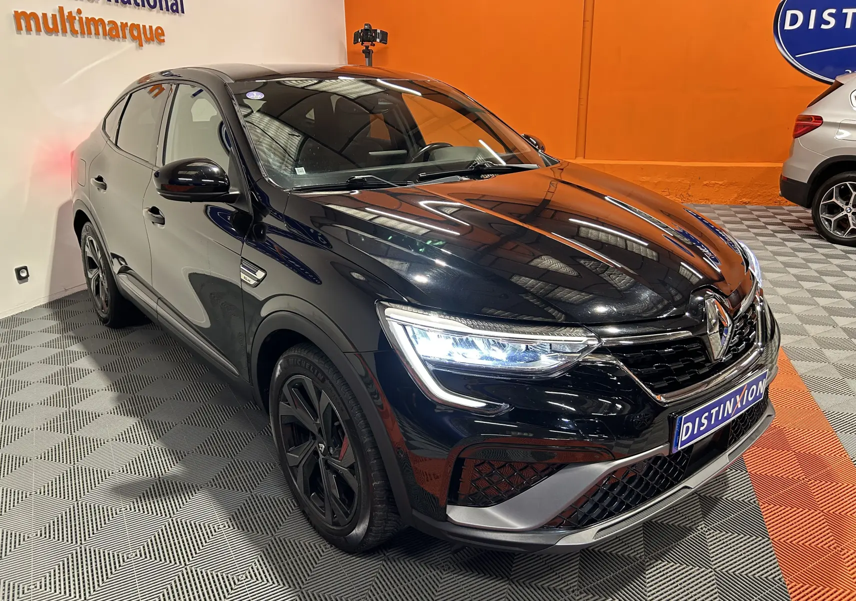 Renault Arkana E-Tech noir en 3/4 avant droit, avec phares LED allumés et jantes noires distinctives.