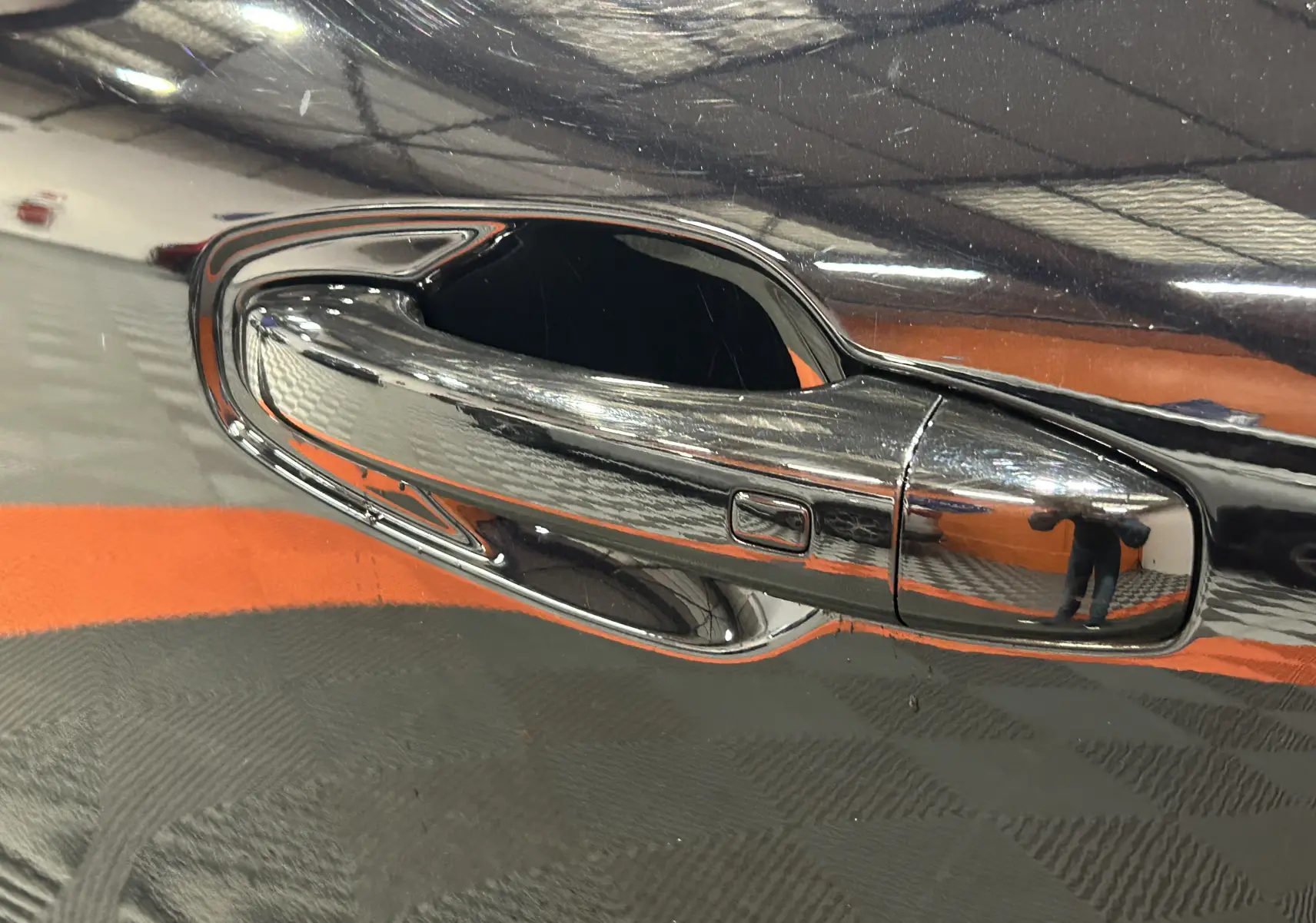 Gros plan sur la poignée de porte chromée d’une Renault Arkana noire, reflet de l’environnement intérieur visible.