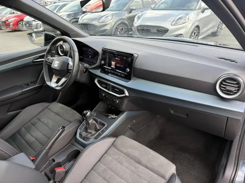 Intérieur du SEAT Arona 2025 vu côté conducteur, tableau de bord moderne avec écran tactile et sellerie noire.