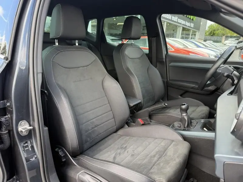 Vue intérieure côté conducteur du SEAT Arona 2025 gris Magnétique Métal, montrant les sièges avant en tissu et alcantara avec boîte manuelle.