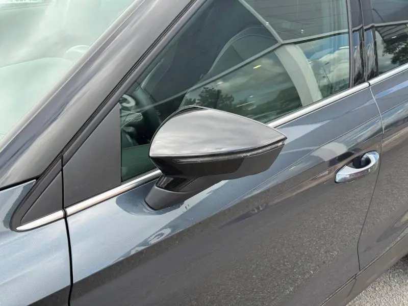 Gros plan sur le rétroviseur côté gauche d’un SEAT Arona 2025 gris magnétique métal avec poignée de porte visible.