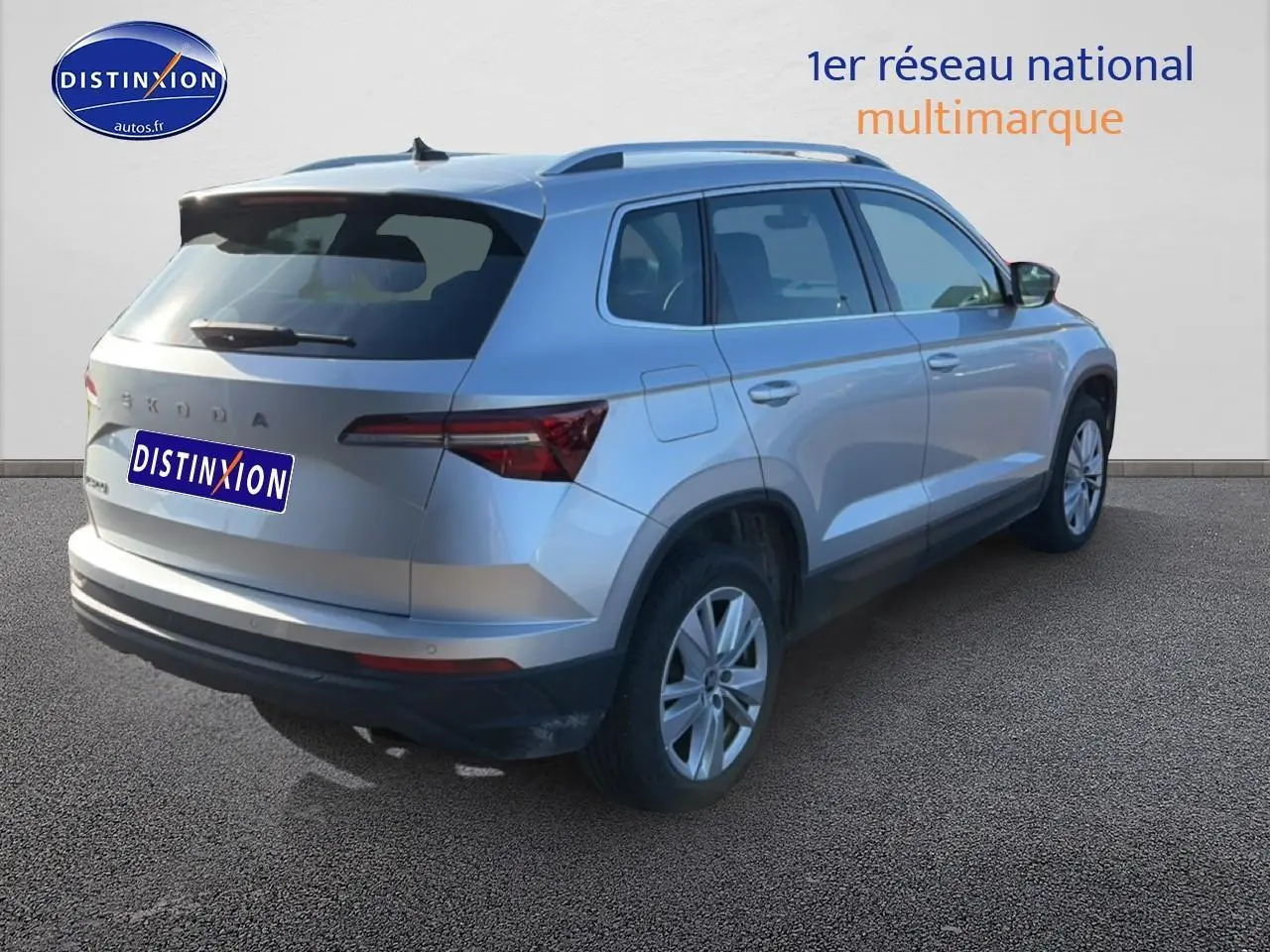 Vue 3/4 arrière droite d'un Skoda Karoq gris avec barres de toit et feux arrière LED sur fond neutre.